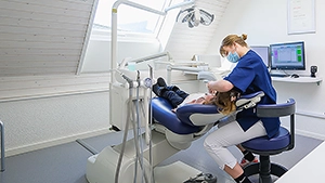 Professionnelle de santé souriante portant un casque, assise à l’accueil du cabinet dentaire